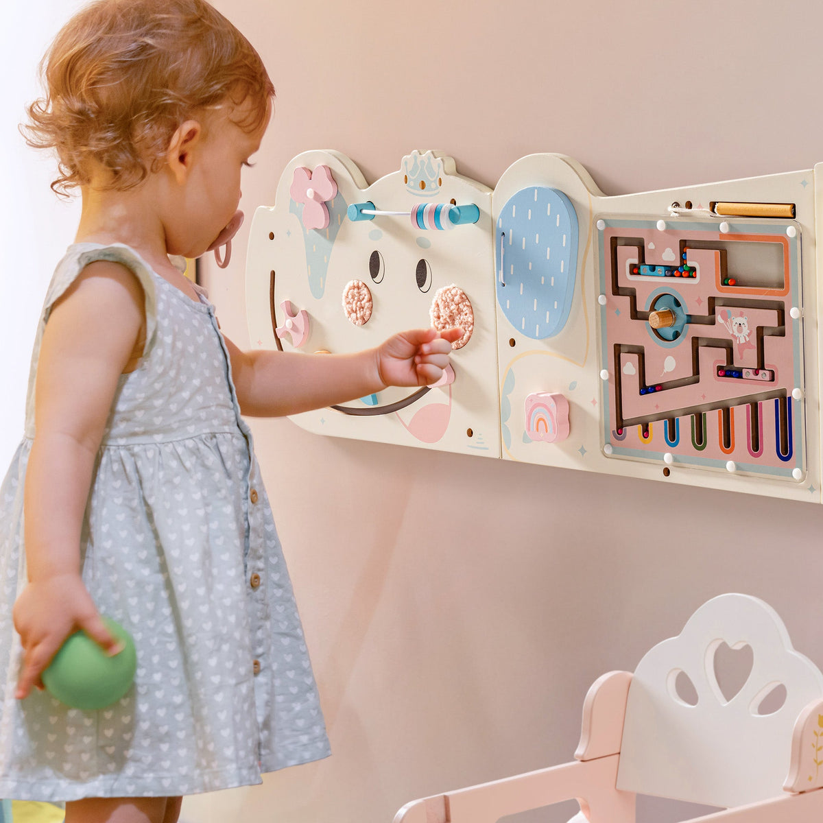 Toddler girl reaching to touch the cream elephant activity busy board mounted on the wall