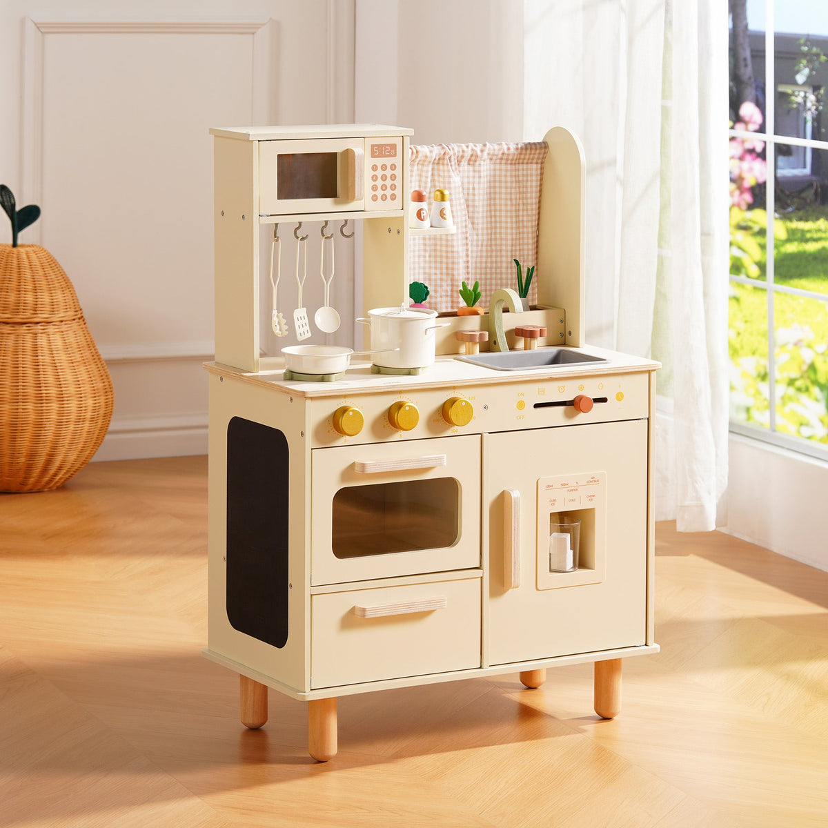 Cream wooden play kitchen with oven, microwave, and pot rail, displayed in a bright sunlit playroom.