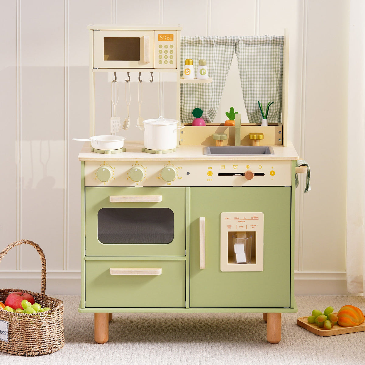 Sage green wooden play kitchen displayed with a wicker fruit basket nearby in a warm, naturally lit playroom setting.