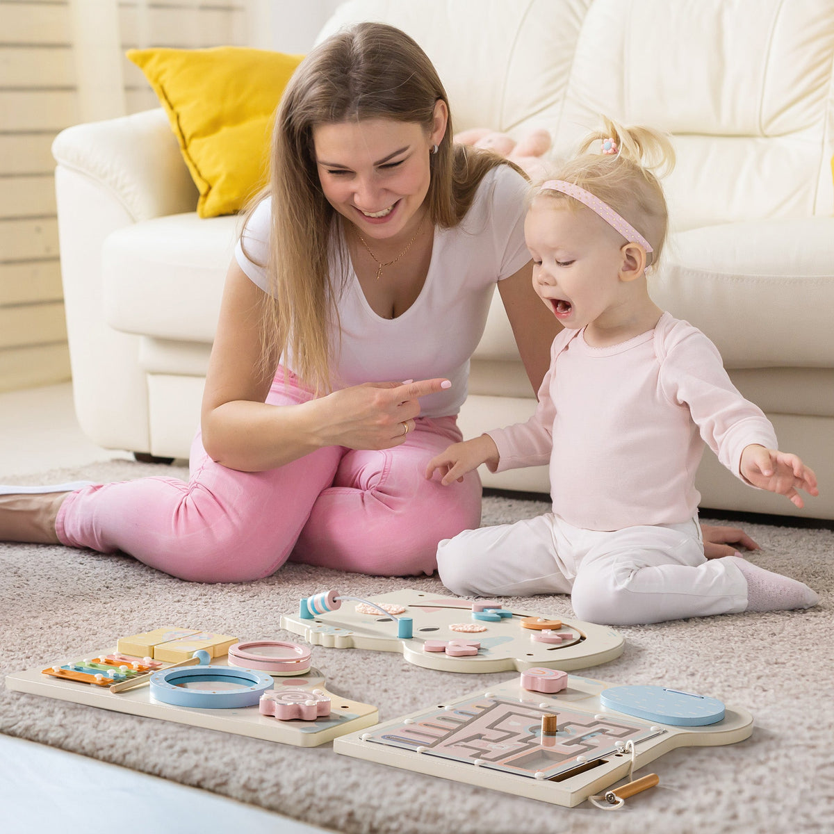 Mother and toddler playing on a floor mat near the cream elephant activity busy board