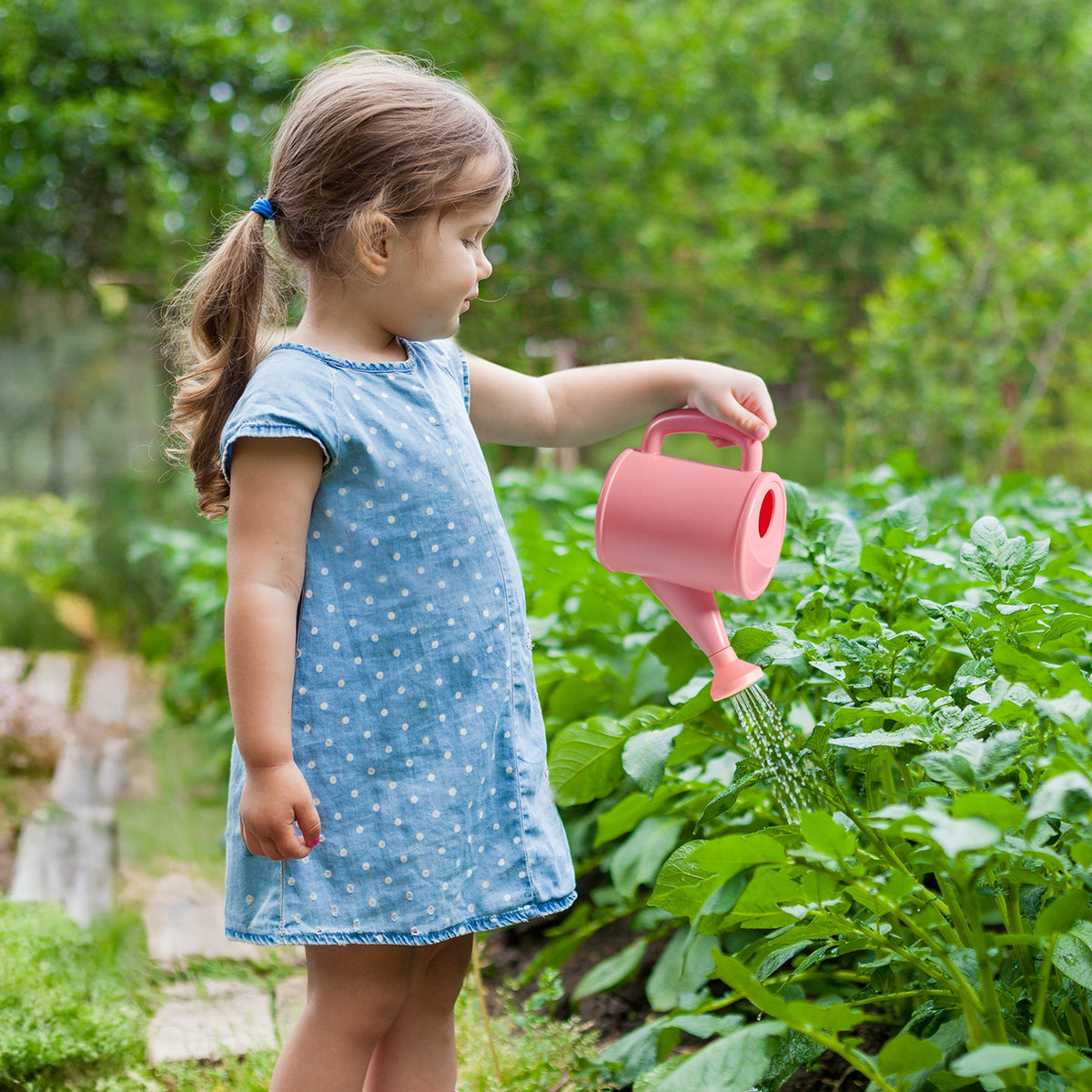 Girl watering garden plants with the rose-pink bow-set watering can