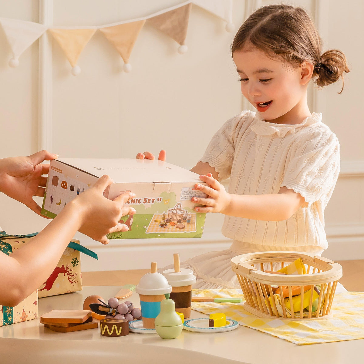 ROBUD Kids Wooden Picnic Play Food Set lifestyle view with girl opening gift box beside basket full of wooden play food and pastry pieces