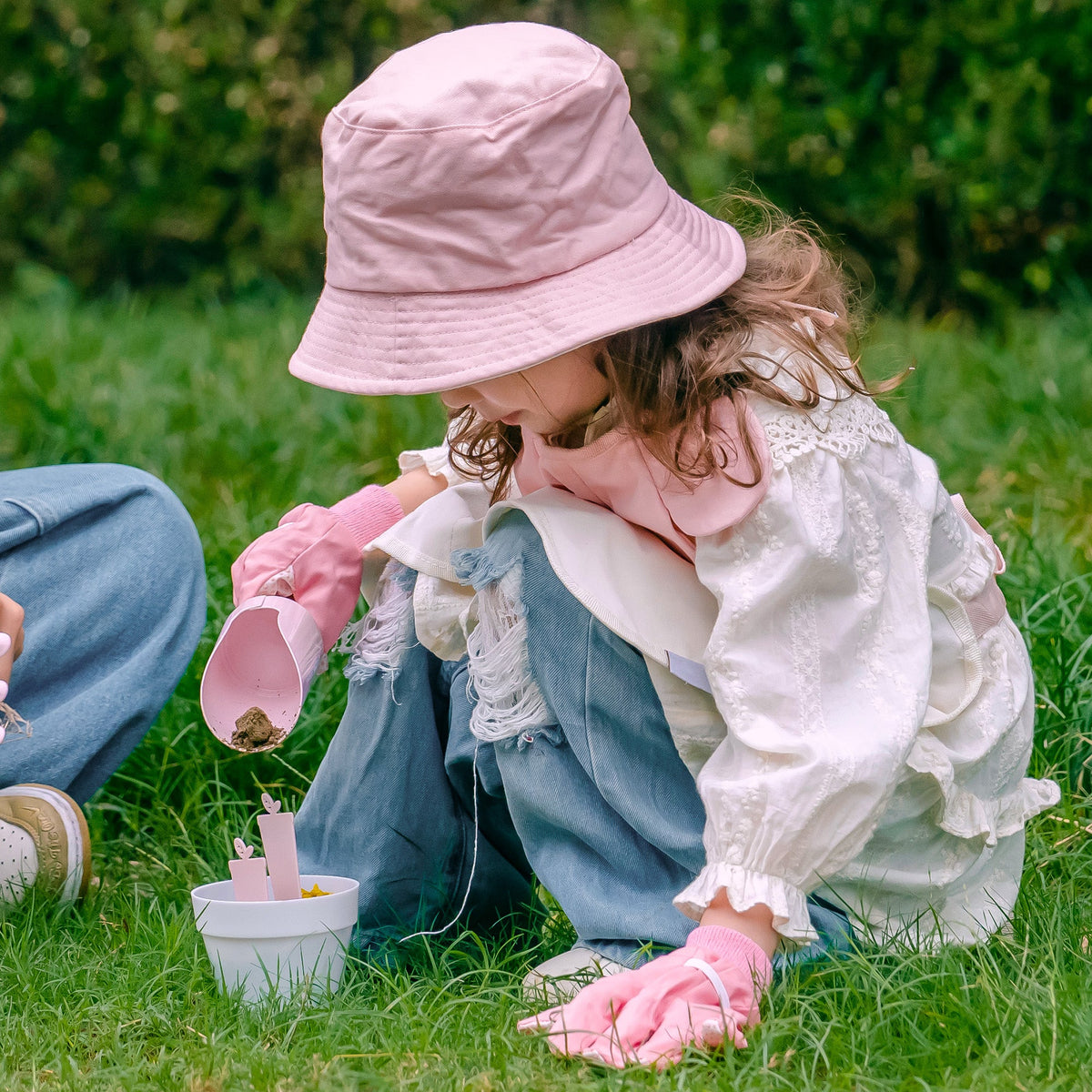 Girl kneeling on grass, pouring water from the light pink watering can