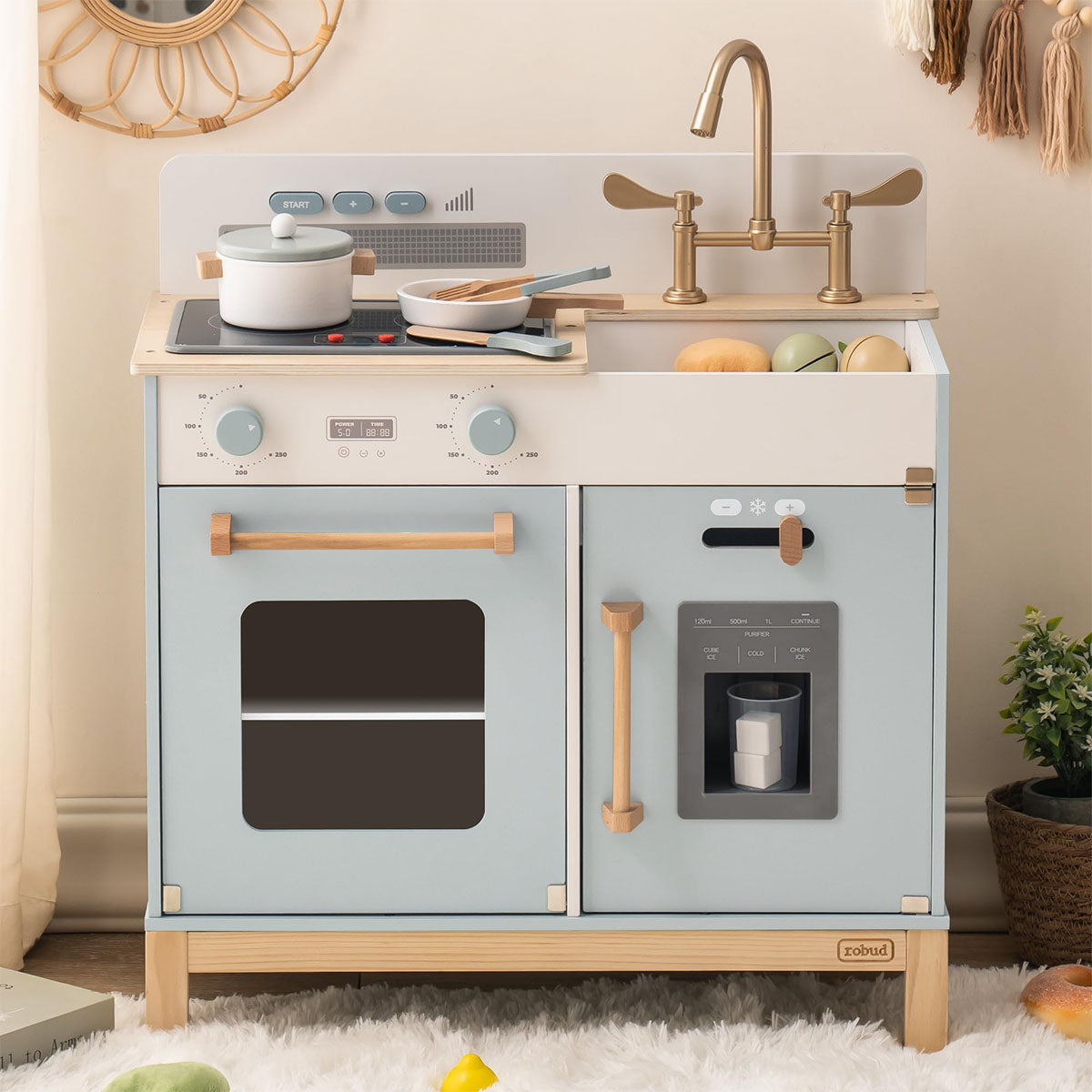 Blue-grey wooden play kitchen with gold faucet and knobs, shown in a home playroom with a round wall mirror