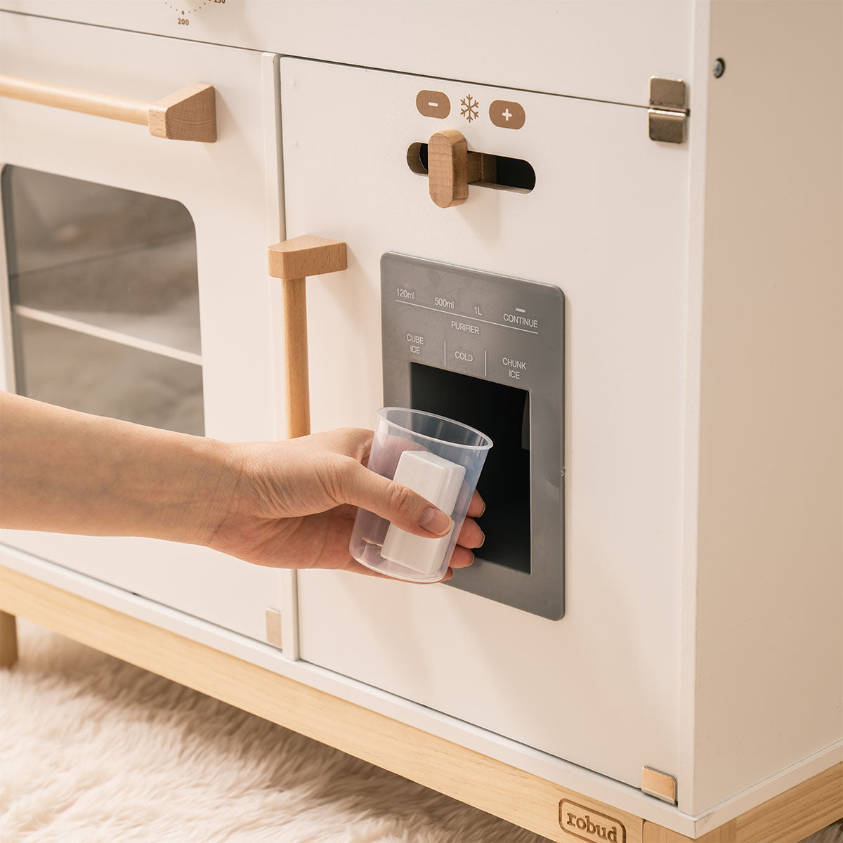 White wooden play kitchen close-up showing the ice and water dispenser panel with cube ice, chunk ice, and cold water controls