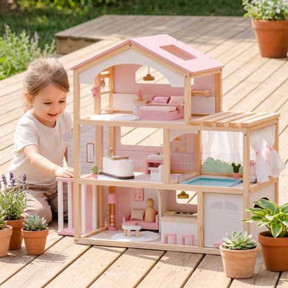 Pink and natural wood three-story open-concept dollhouse outdoors on a deck, a wooden peg doll on the living-room sofa, a child about 4 years old reaching toward the external elevator