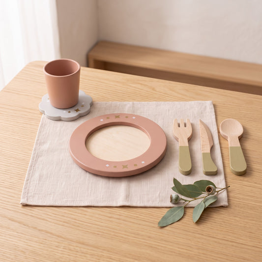 A wooden play place setting with a rose plate, terracotta cup, flower coaster and sage-handled cutlery on a linen napkin