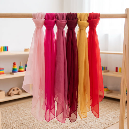 Pale pink, magenta, dusty rose, wine red, mustard gold and red play silks draped together on a wooden rack